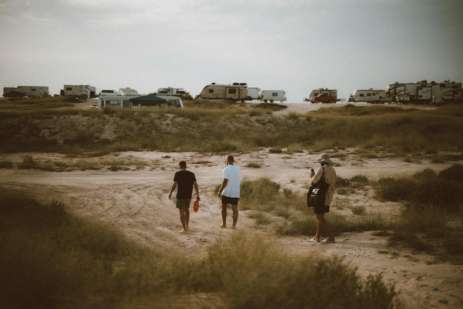 Three people walk among recreational vehicles in a desert setting in Dubai. Adventure travel and exploration.